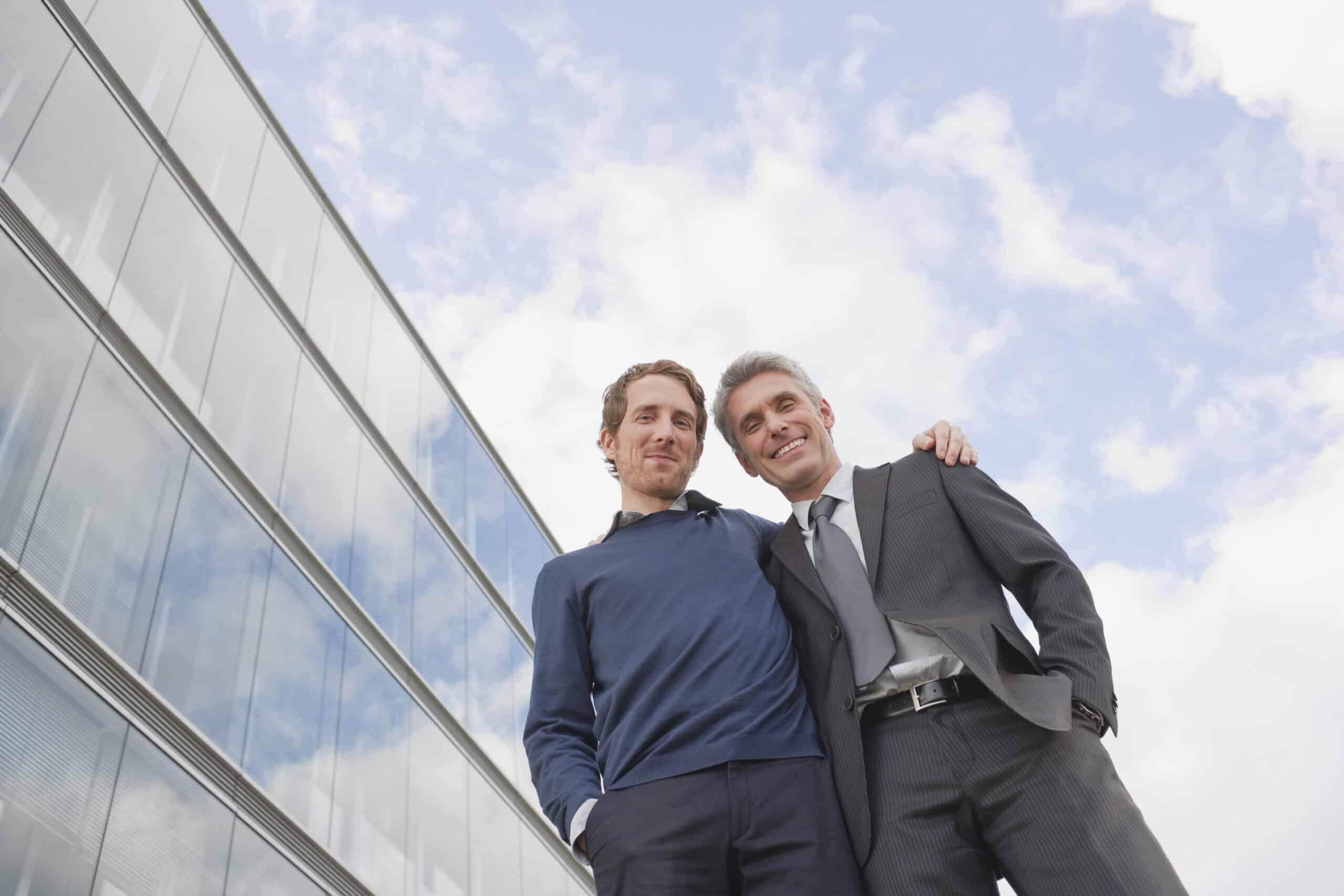 Zwei Männer in partnerschaftlicher Pose vor einem Firmengebäude.
